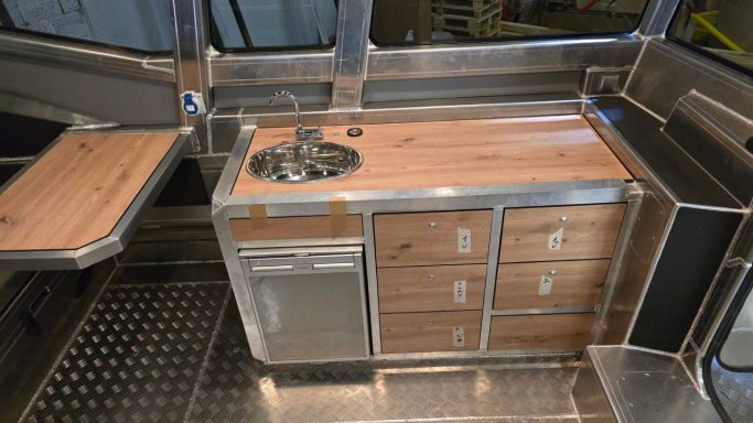 Küchenzeile mit Holzarbeitsplatte, Spüle und mehreren Schubladen in einem modernen Camper.