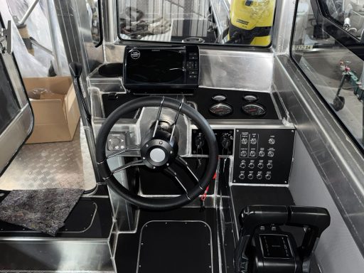 Steuerstand eines Bootes mit Steuer, Bedienelementen und Laptop.