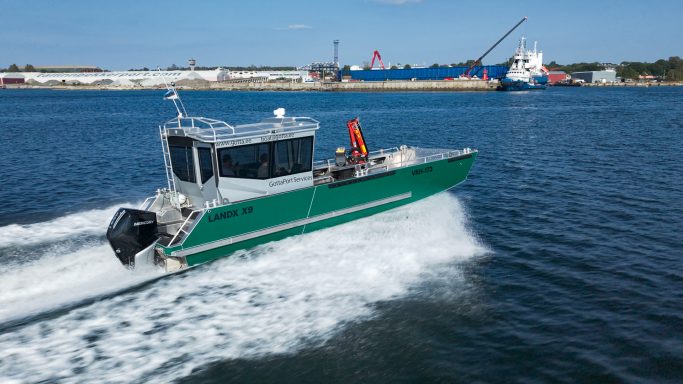 Schnelles grünes Boot fährt durch Wasser, mit Hafen und Schiff im Hintergrund.