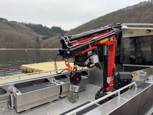 Kranausrüstung auf einem Boot am Wasser, im Hintergrund bewaldete Hügel.
