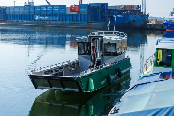 Ein grünes Schiff liegt ruhig im Wasser, umgeben von Containern am Hafen.