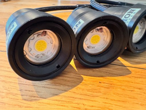 Drei schwarze LED-Lampen mit runden Lichtern auf einem Holzuntergrund.